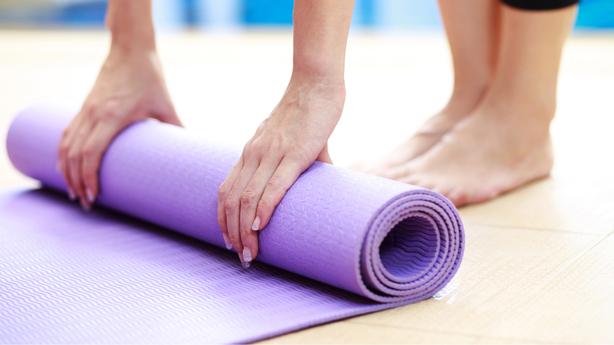 Purple yoga mat being rolled up on the floor.