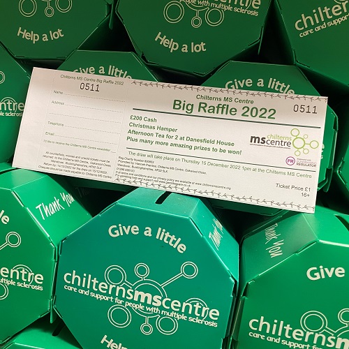 Selection of green money boxes showing the logo for the Chilterns MS Centre. Resting on the money boxes is a book of raffle tickets.