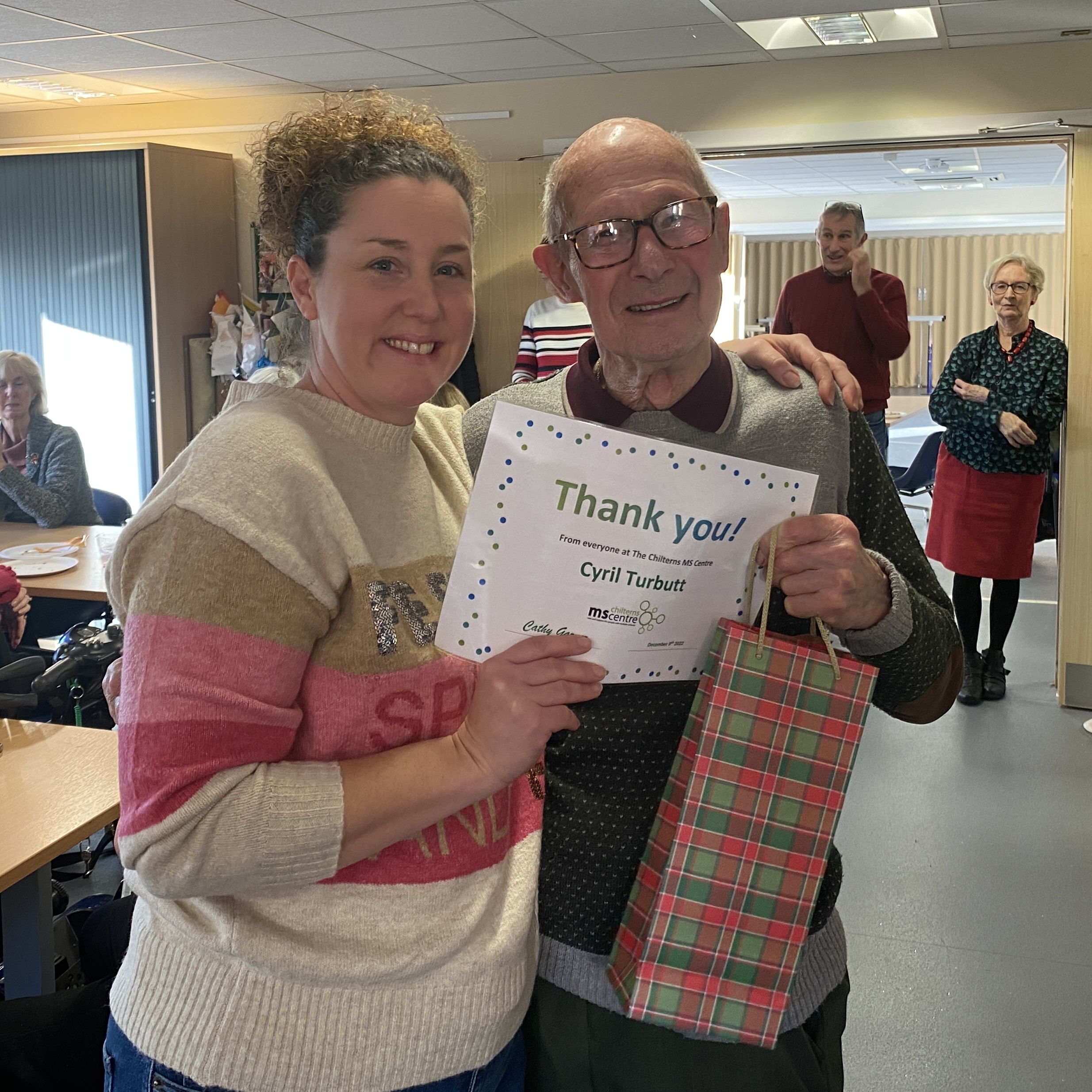 Smiling man holding up a certificate saying thank you. By his side is a younger lady, also smiling.