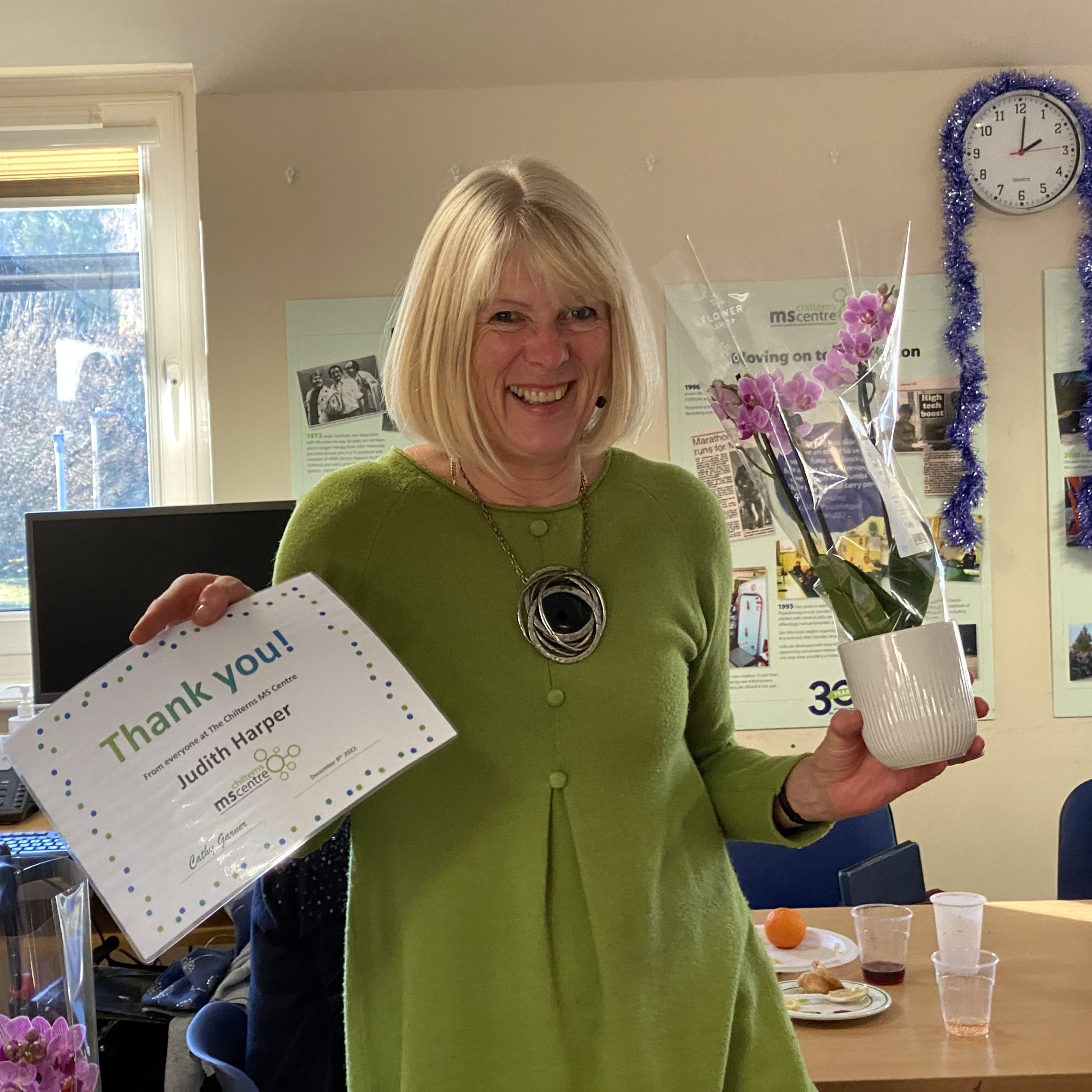 Smiling lady holding up a certificate saying thank you in one hand and a flower in the other.