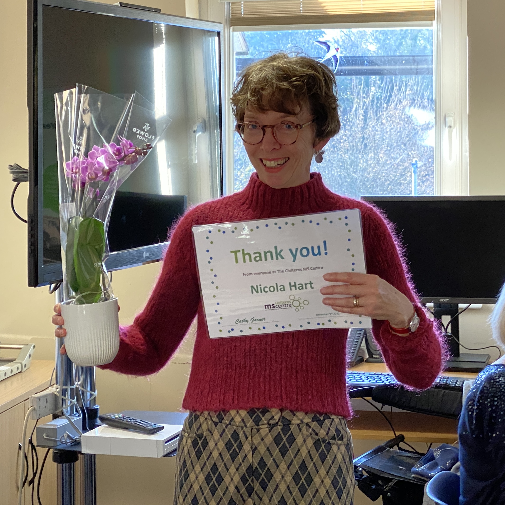 Smiling lady holding up a certificate saying thank you in one hand and a flower in the other.