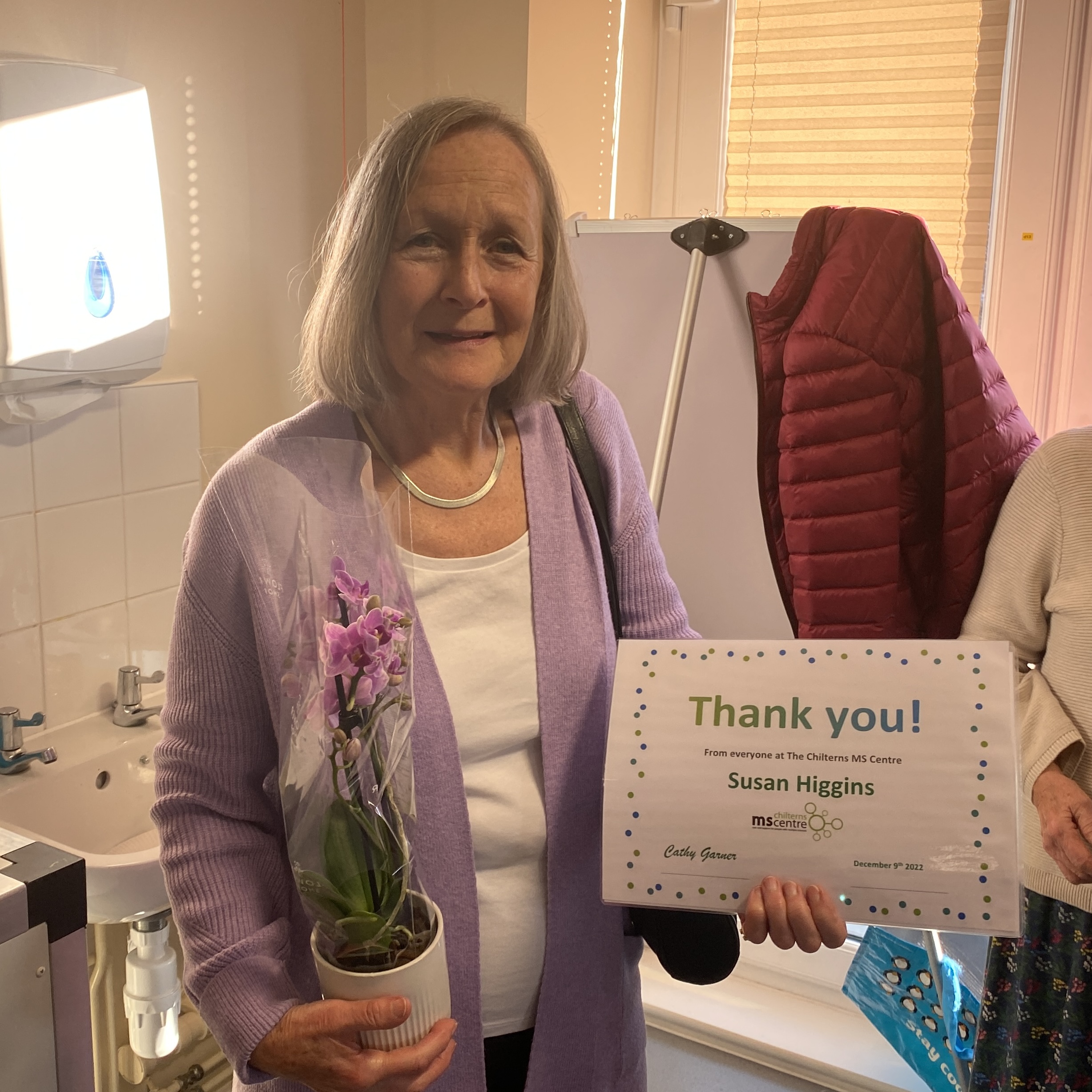 Smiling lady holding up a certificate saying thank you in one hand and a flower in the other.