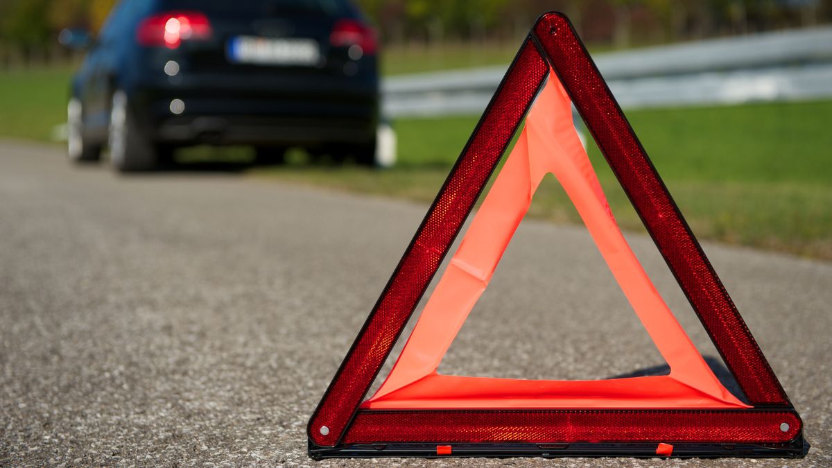 Red triangular warning sign placed behind a broken down car