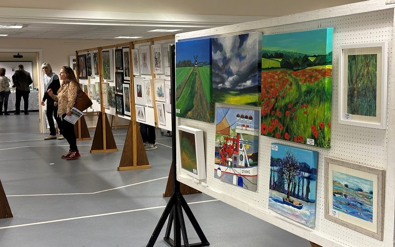 View of an art exhibition with paintings on the wall and on central frames.