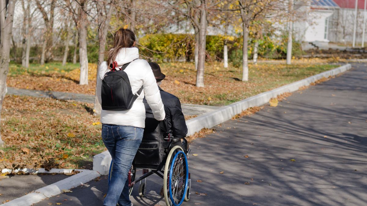 Rear view of a lady pushing a wheelchair through a park,