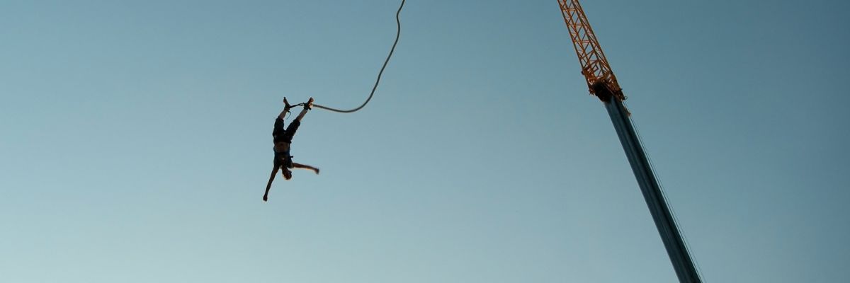 Person falling from a high up crane. Their ankles are attached to a bungee chord which is attached to the crane.