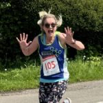 Smiling woman taking part in a running race. She is waving her hands in the air.